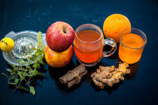 Close-up of herbal and organic juice of apple with orange juice, cinnamon sticks, lemon juice, ginger or adrak, and some tulsi leaves or holy basil leaves in a transparent glass with all raw ingredients.