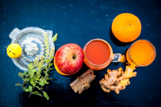 Close-up of herbal and organic juice of apple with orange juice, cinnamon sticks, lemon juice, ginger or adrak, and some tulsi leaves or holy basil leaves in a transparent glass with all raw ingredients.