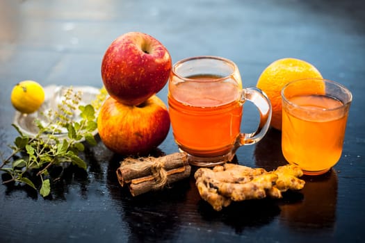 Close-up of herbal and organic juice of apple with orange juice, cinnamon sticks, lemon juice, ginger or adrak, and some tulsi leaves or holy basil leaves in a transparent glass with all raw ingredients.