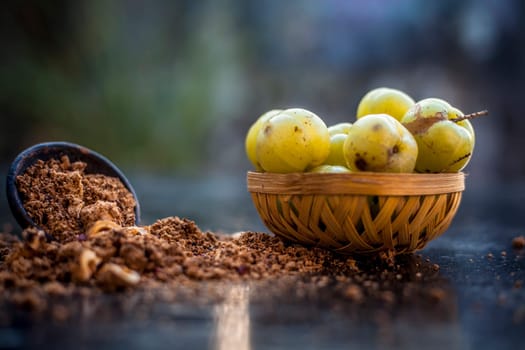 Close-up of raw amla or Phyllanthus emblica or Indian gooseberry in a fruit basket with its dried seed powder in a clay bowl used in a face pack, drinks, and natural medicines on the wooden surface.