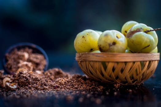 Close-up of raw amla or Phyllanthus emblica or Indian gooseberry in a fruit basket with its dried seed powder in a clay bowl used in a face pack, drinks, and natural medicines on the wooden surface.