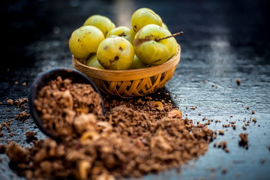 Close-up of raw amla or Phyllanthus emblica or Indian gooseberry in a fruit basket with its dried seed powder in a clay bowl used in a face pack, drinks, and natural medicines on the wooden surface.