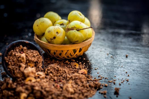Close-up of raw amla or Phyllanthus emblica or Indian gooseberry in a fruit basket with its dried seed powder in a clay bowl used in a face pack, drinks, and natural medicines on the wooden surface.
