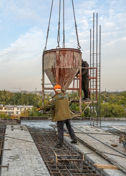 The workers on a building infrastructure roof with machinery and tools. Pouring concrete into a mold