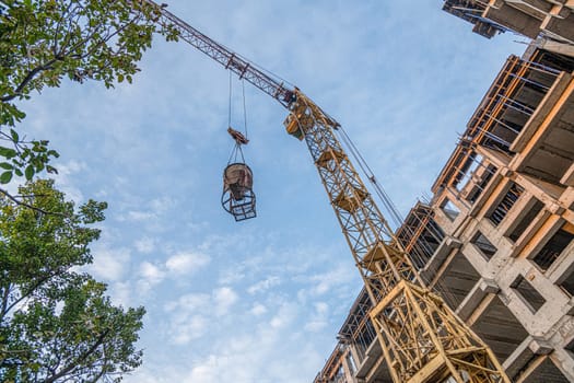 A low angle shot of a crane with equipment on a construction site with a new building infrastructure. Pouring concrete into a mold