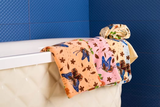 A row of colorful patterned towels hanging on the side of a bathtub