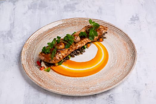 A closeup shot of a Fish course with salmon meat, herbs and orange sauce on a marble plate