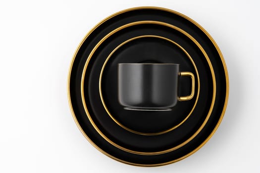 A set of black and golden ceramic plates and cup on a white background. Top view