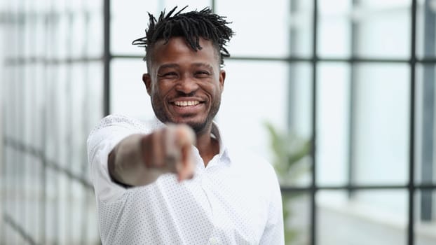 Handsome happy young man in white shirt pointing at camera