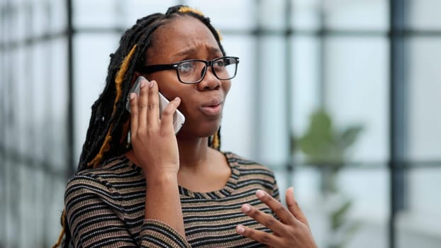 Close up portrait black woman employee in glasses working in office talking on mobile phone solving business issues distantly.