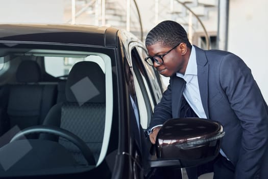 Opening the door. Young african american businessman in black suit is the autosalon.