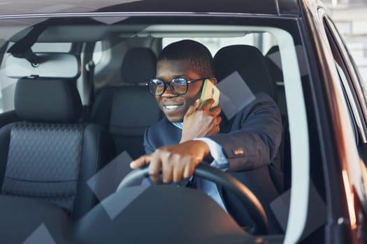 Front view. Young african american businessman in black suit is in the automobile.