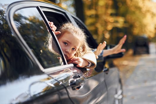 Little girl with her brother sitting in the car and looking through the opened window.