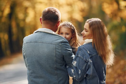 Little girl with her parents. Happy family is in the park at autumn time together.