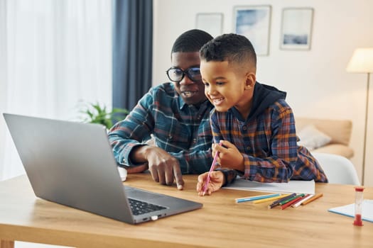 With laptop on table. African american father with his young son at home.