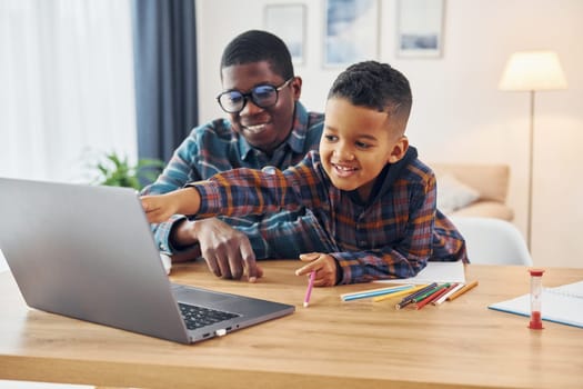 With laptop on table. African american father with his young son at home.