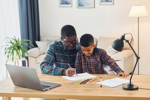 With laptop on table. African american father with his young son at home.