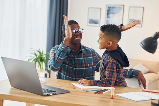 Using laptop. African american father with his young son at home.