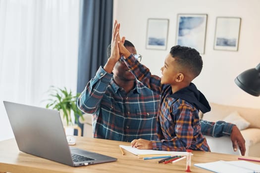 Using laptop. African american father with his young son at home.