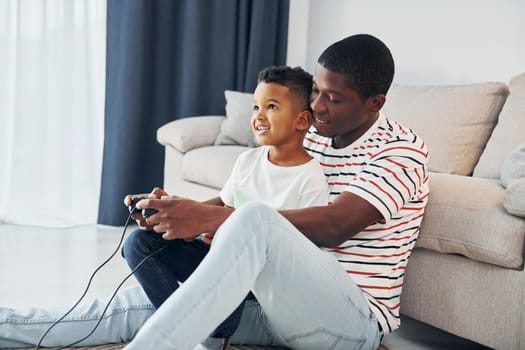 Playing video games. African american father with his young son at home.