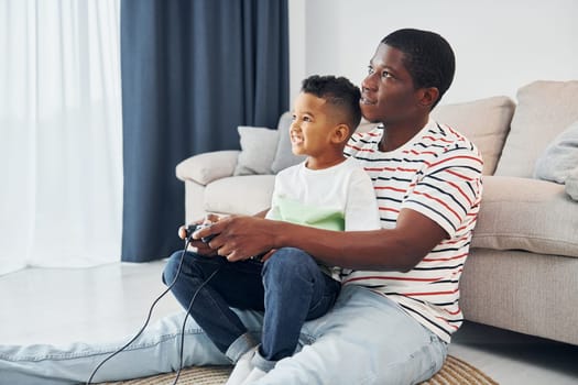 Playing video games. African american father with his young son at home.