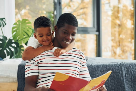 Reading book. African american father with his young son at home.