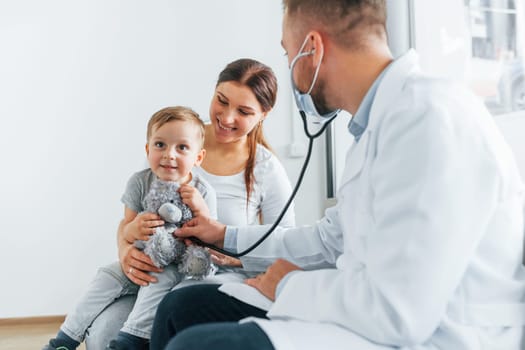 The little boy is being examined. Two doctors in white coats is in the clinic working together.