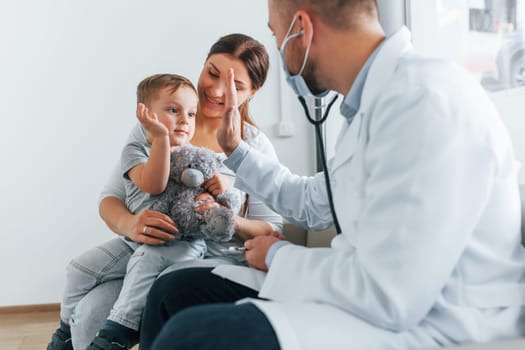 The little boy is being examined. Two doctors in white coats is in the clinic working together.