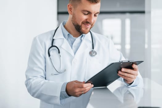 Holding notepad. Professional medic in white coat is in the clinic.