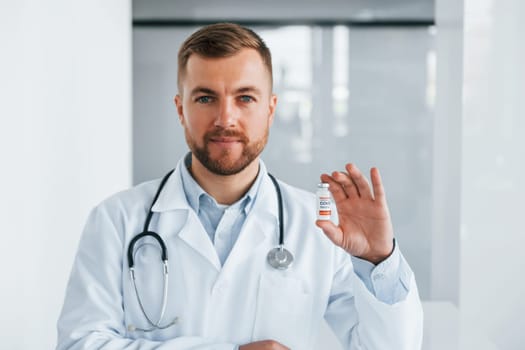 With COVID-19 vaccine. Professional medic in white coat is in the clinic.