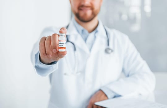 With COVID-19 vaccine. Professional medic in white coat is in the clinic.