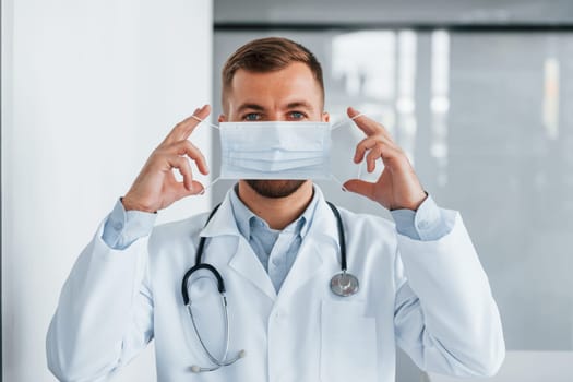 Holding mask. Professional medic in white coat is in the clinic.