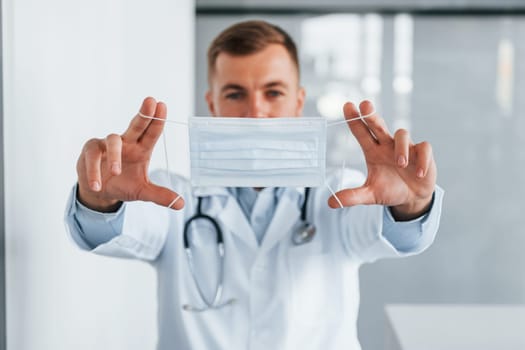 Holding mask. Professional medic in white coat is in the clinic.