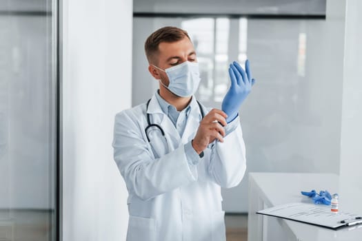 In blue gloves. Professional medic in white coat is in the clinic.
