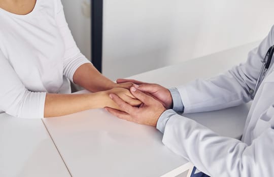 Holding customer by the hands. Professional medic in white coat is in the clinic.