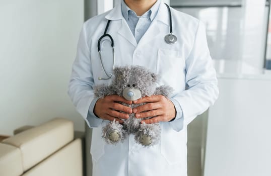 With teddy bear. Professional medic in white coat is in the clinic.