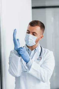 In blue gloves. Professional medic in white coat is in the clinic.