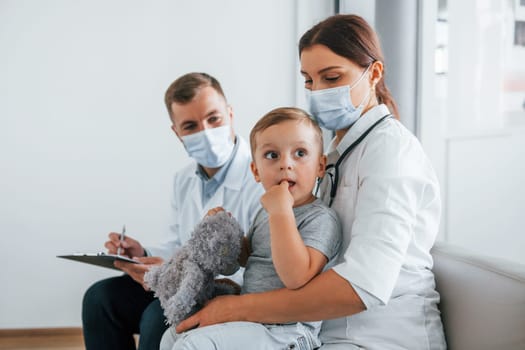 Little boy is in the clinic. Two doctors in white coats is in the hospital working together.