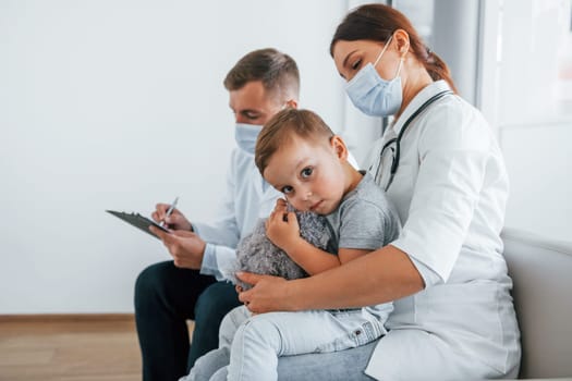 Little boy is in the clinic. Two doctors in white coats is in the hospital working together.