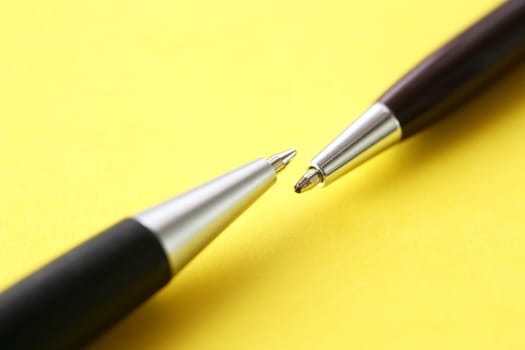 Two pens opposite each other on yellow paper background