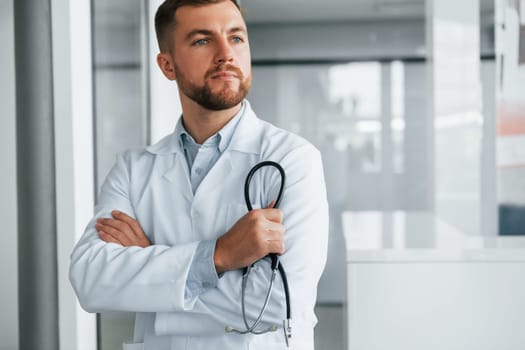 Holding stethoscope. Professional medic in white coat is in the clinic.