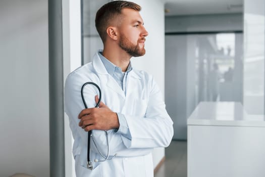 Holding stethoscope. Professional medic in white coat is in the clinic.