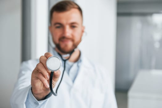 Holding stethoscope. Professional medic in white coat is in the clinic.