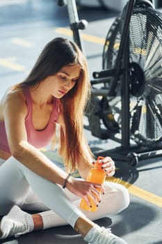 Sitting with bottle of water. Beautiful young woman with slim body type is in the gym.