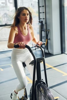 On exercise bike. Beautiful young woman with slim body type is in the gym.