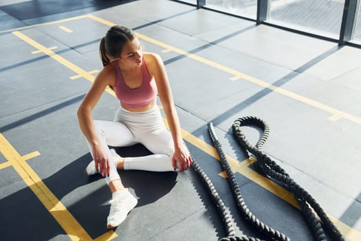 Sitting with rope. Beautiful young woman with slim body type is in the gym.
