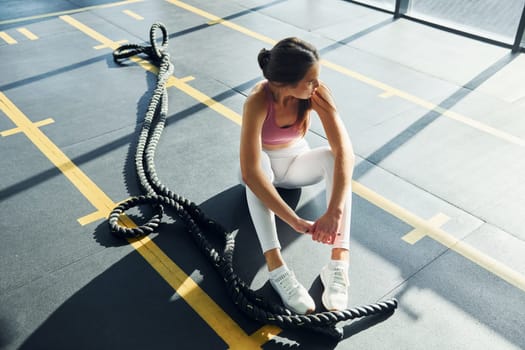Sitting with rope. Beautiful young woman with slim body type is in the gym.