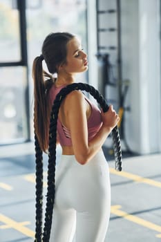 Standing and holding exercise equipment. Beautiful young woman with slim body type is in the gym.