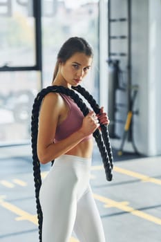 Standing and holding exercise equipment. Beautiful young woman with slim body type is in the gym.