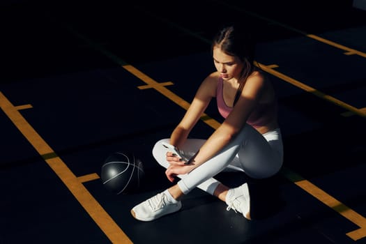 Sitting with fitness ball. Beautiful young woman with slim body type is in the gym.